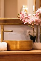 Un tocador de baño con lavamanos dorado, un espejo y orquídeas rosadas.