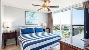 A hotel room with a bed, a ceiling fan, a large window with a view, a nightstand, and a desk. - Terrace At Pelican Beach 602 2 Bedroom Home (Destin)