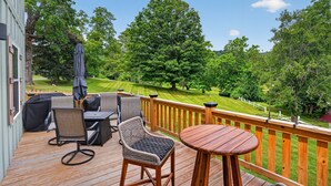 A wooden deck with outdoor furniture, a grill, and a view of a green landscape with trees. - Mountain Views Basecamp West Jefferson 2 Bedroom Home (West Jefferson)