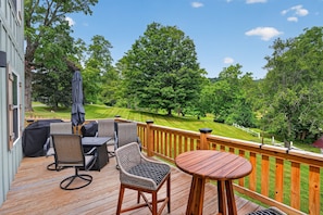 A wooden deck with outdoor furniture, a grill, and a view of a green landscape with trees. - Mountain Views Basecamp West Jefferson 2 Bedroom Home (West Jefferson)