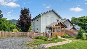 A two-story house with a porch, a wooden fence, and a gravel driveway. - Mountain Views Basecamp West Jefferson 2 Bedroom Home (West Jefferson)
