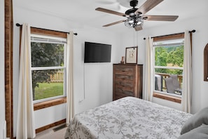 A bedroom with a bed, a ceiling fan, a TV, and windows with curtains. - Mountain Views Basecamp West Jefferson 2 Bedroom Home (West Jefferson)