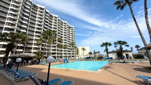 Un hotel con una piscina grande, palmeras y cielo despejado.