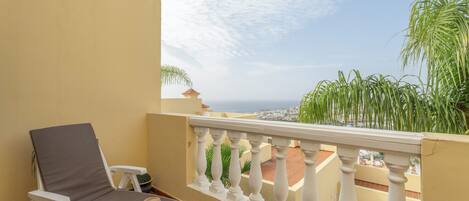 A balcony with a white balustrade, a white lounge chair, a hat, and a book.