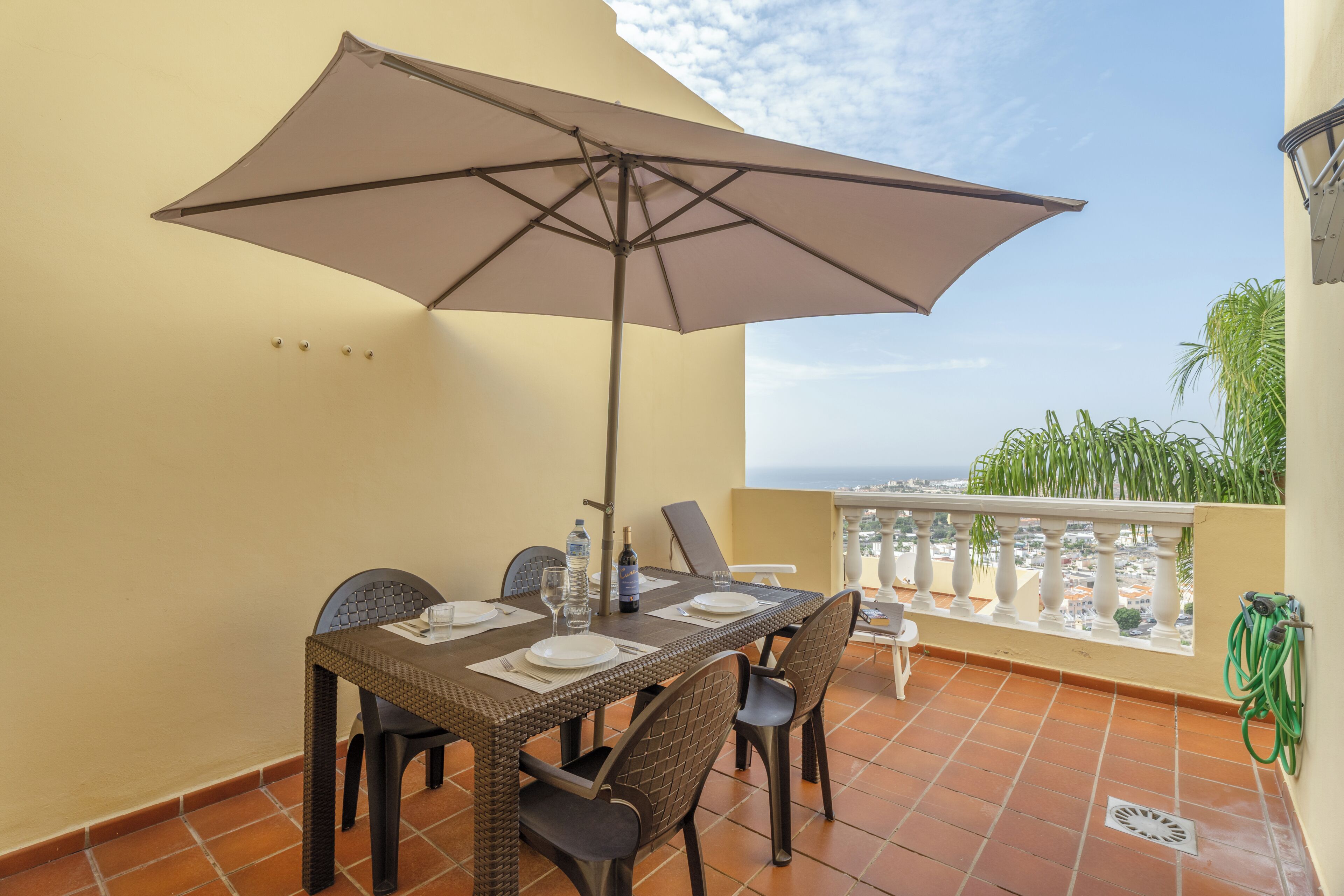 A balcony with a table set for two, a large umbrella, and a view of the city.