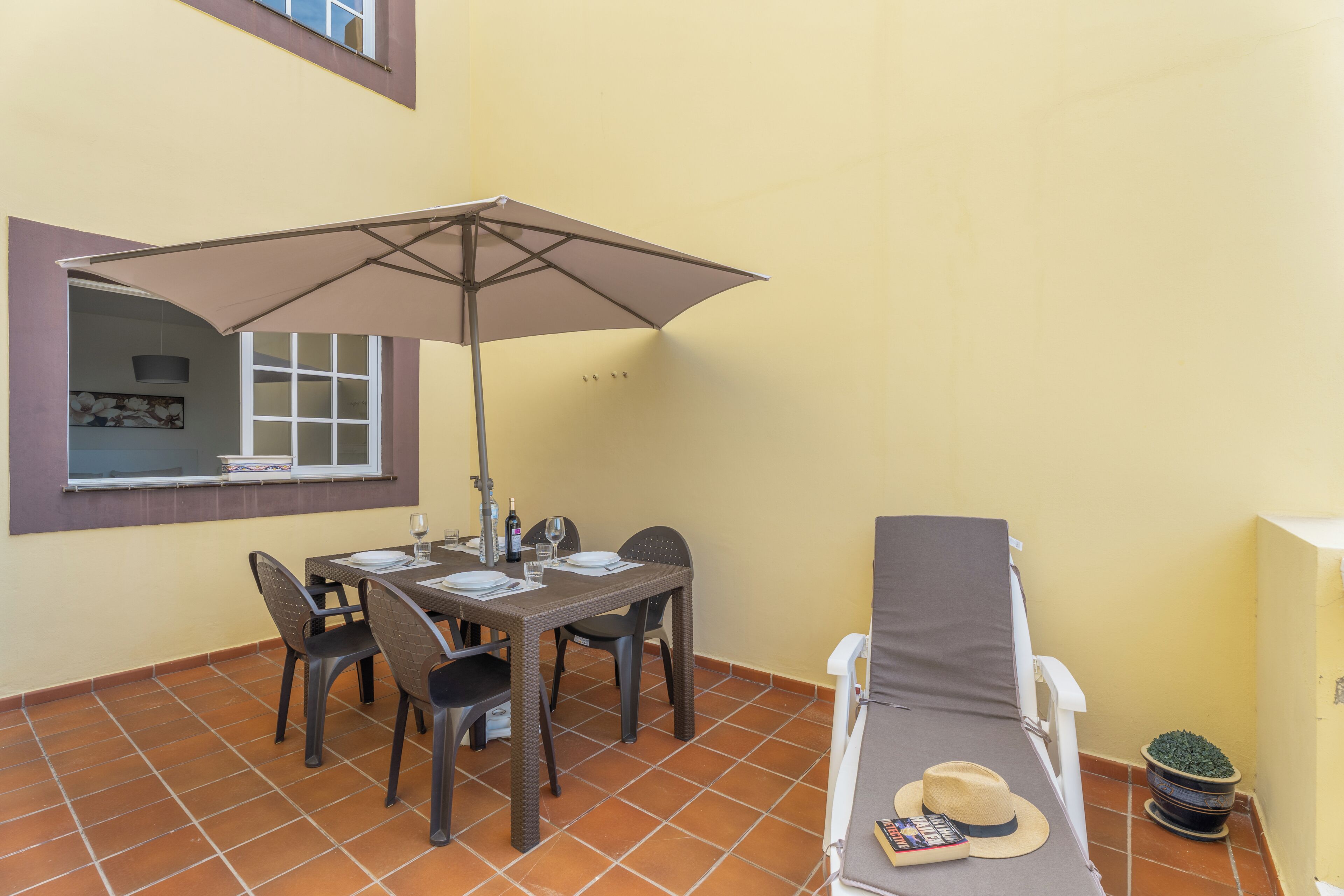 Un patio con una mesa, sillas, una sombrilla, una silla de descanso y una planta en maceta.
