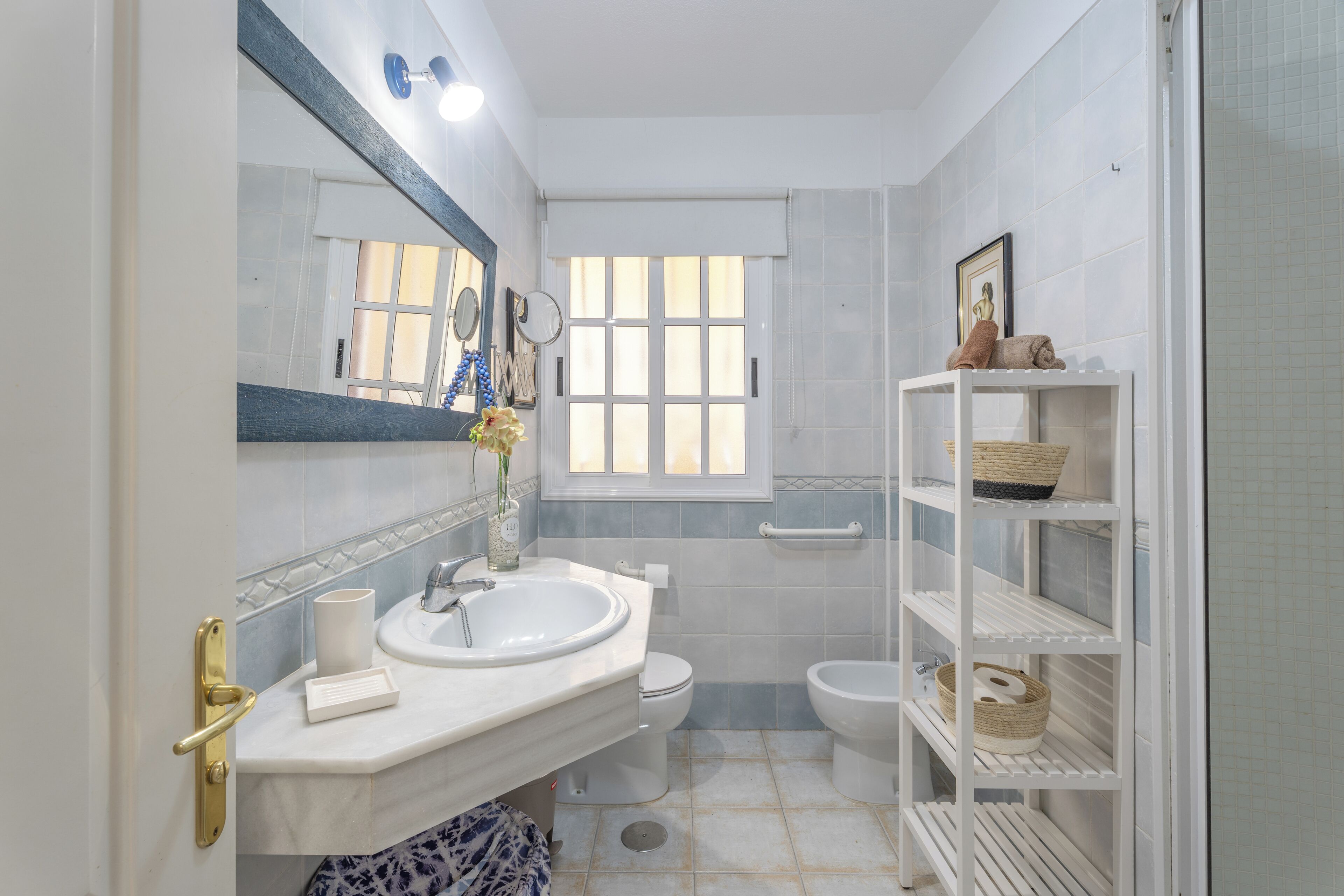 A bathroom with a sink, toilet, bidet, and a shelf with baskets.