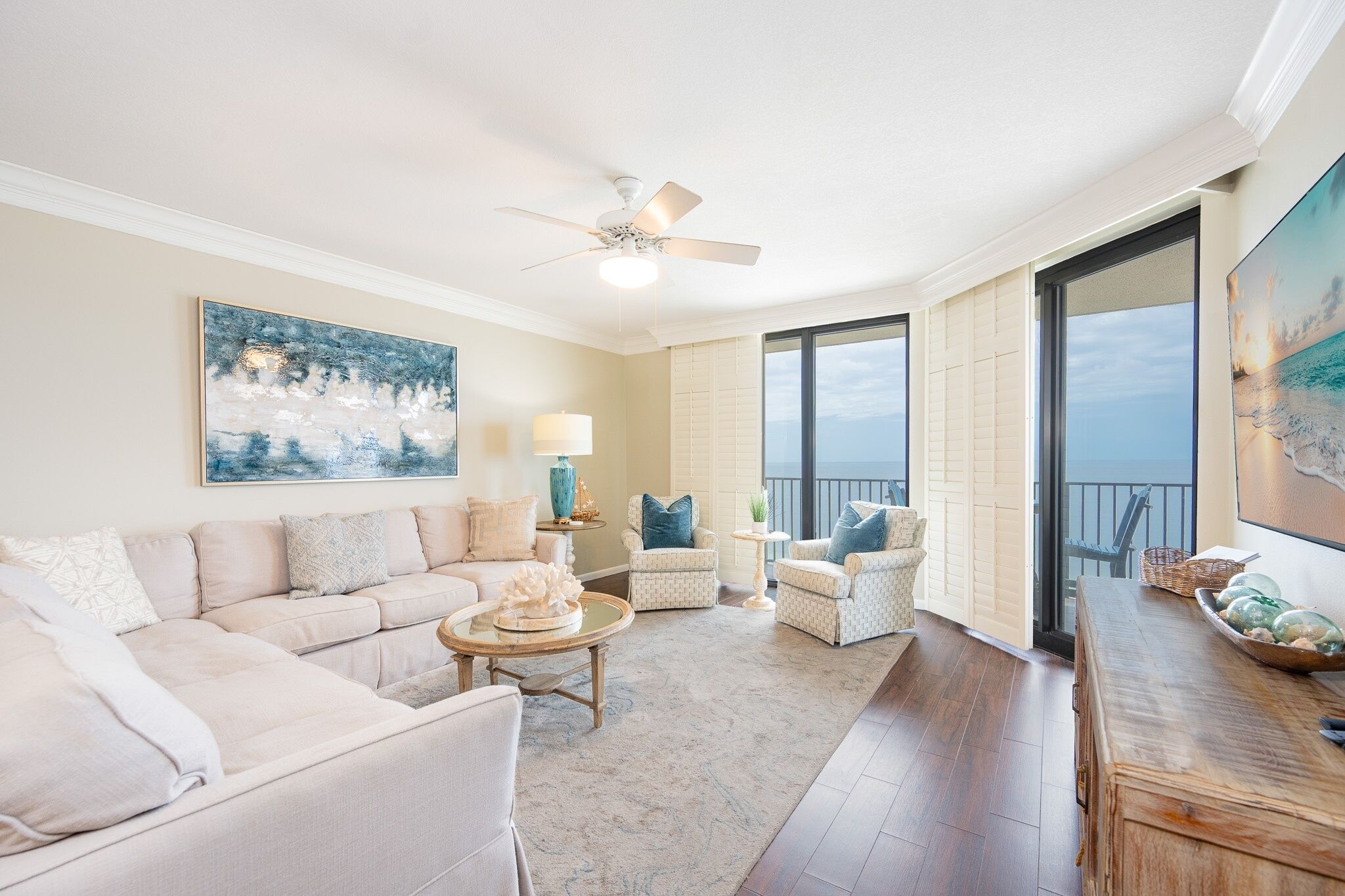 A spacious living room with a large window, a ceiling fan, and a view of the ocean.