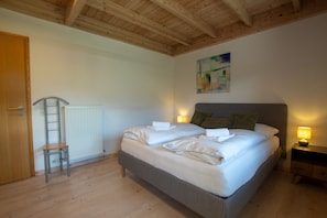 Ein Schlafzimmer mit Holzboden, einem Bett mit weißen Leinen, einem Heizkörper, einer Leiter und einem Nachttisch mit Lampe.