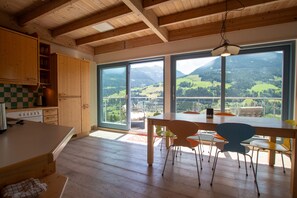 Eine Küche mit Holzausstattung, einem Esstisch mit Stühlen und großen Fenstern mit Blick auf die Berge.