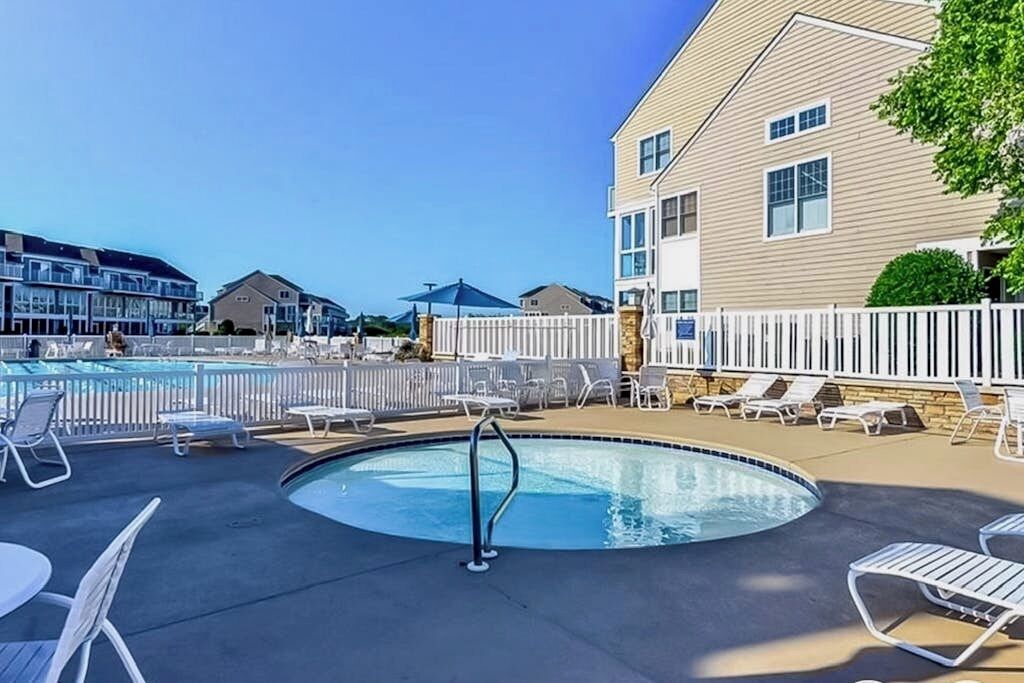 A swimming pool with lounge chairs and a white fence.