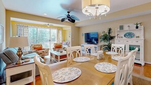 A living room with a dining table, chairs, a TV, and a ceiling fan.