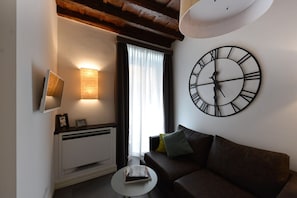 Ein Wohnzimmer mit einer großen Wanduhr, einem Sofa, einem kleinen Tisch und einer Heizung.