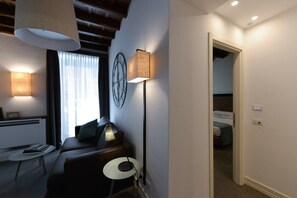 Une chambre d’hôtel moderne avec un canapé, une petite table, une lampe et un lit dans la pièce adjacente.