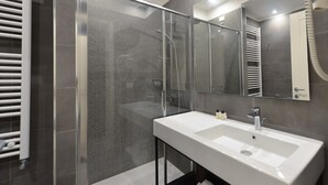 Et moderne badeværelse med et glasbadeværelsesafskærmning, en hvid vask og et stort spejl.