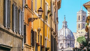 Une rue étroite bordée de bâtiments historiques, un lampadaire et, au fond, la coupole imposante d’une église.