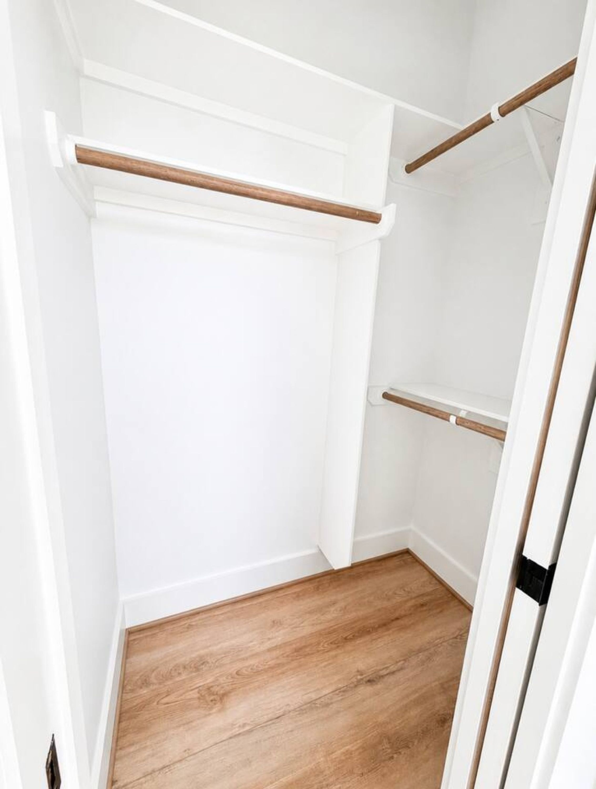 Een inloopkast met witte wanden, houten vloeren en twee houten kledingroedes.