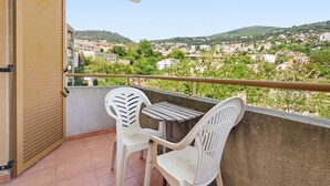 Un balcone con due sedie di plastica bianca e un tavolo, con vista su una cittadina collinare.