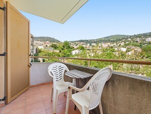 Ein Balkon mit zwei weißen Plastikstühlen und einem Tisch, mit Blick auf eine Stadt am Hang.