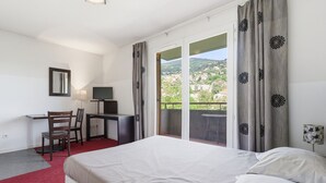 Camera d'albergo con un letto, una scrivania con una sedia, una televisione e un balcone con tende.