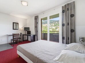 Ein Hotelzimmer mit Bett, Schreibtisch mit Stuhl, Fernseher und einem Balkon mit Vorhängen.