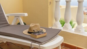 Una tumbona con sombrero y un libro, una barandilla blanca y vistas a edificios.