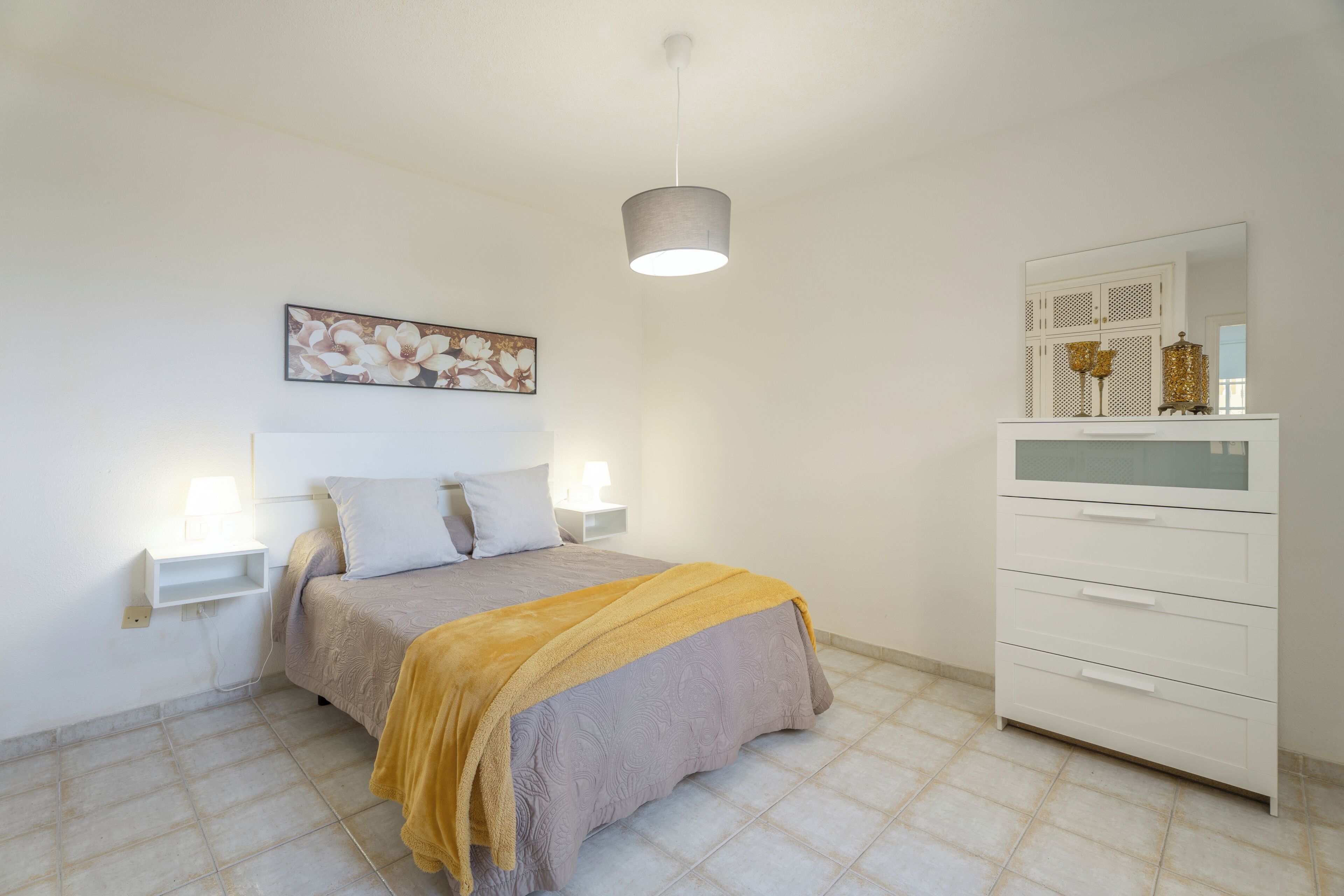Quarto com cama, abajures, cômoda e luminária pendente.