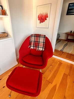 Una silla roja con una manta escocesa, suelo de madera y un cuadro en la pared.
