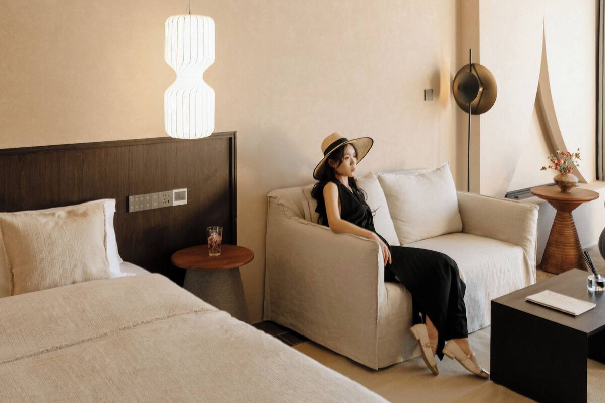 Habitación de hotel con cama, sofá, mesa de centro, lámpara y aplique de pared.