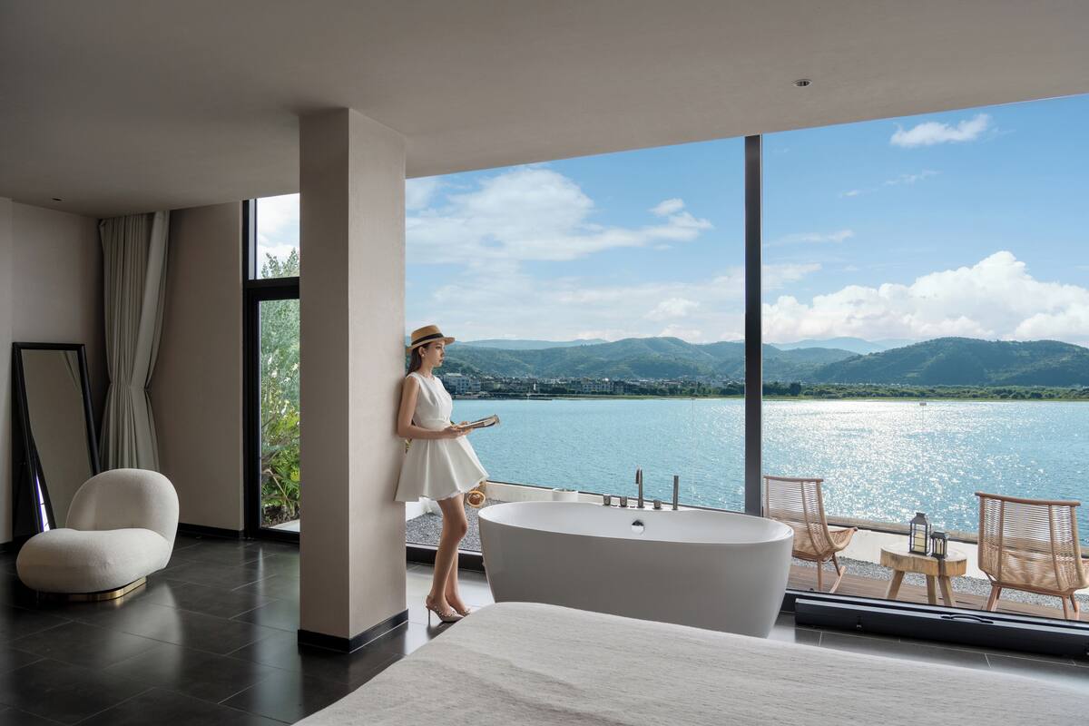 Un baño moderno con una bañera grande, un sofá y vistas a un lago y montañas.