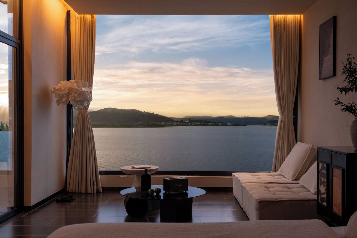 Una habitación moderna con un ventanal grande, un sofá, una mesita y un jarrón decorativo.