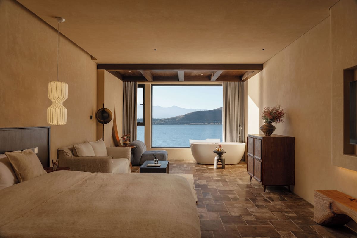 Un dormitorio con una cama grande, un sofá, una mesita y una bañera, con vista al agua.