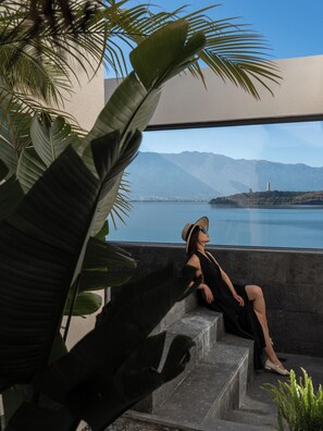 A person sitting on outdoor steps with a view of a body of water and mountains.