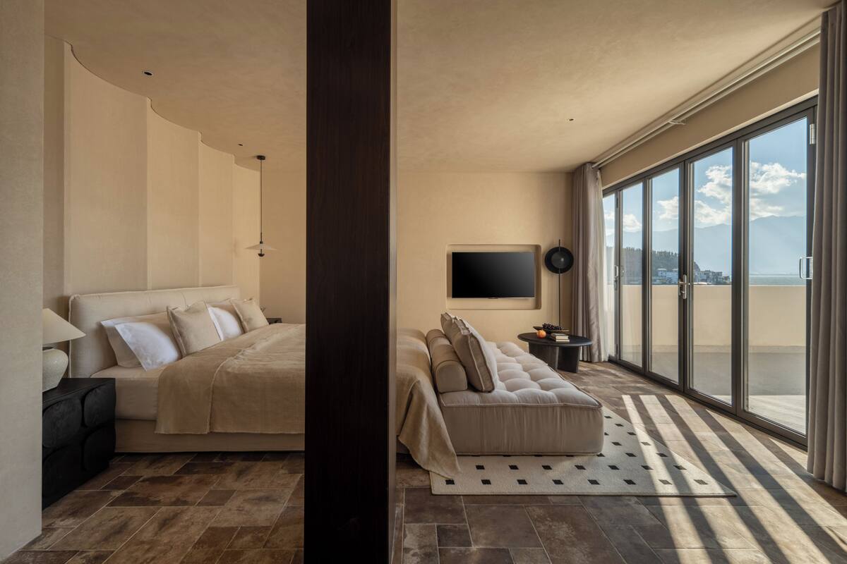 Un dormitorio moderno con una cama grande, un sofá, un televisor y un balcón con vistas.