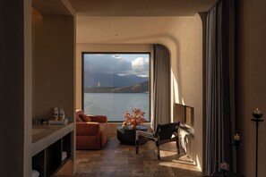 A room with a large window, a sofa, a chair, a small table with decorative items, and a candle holder.