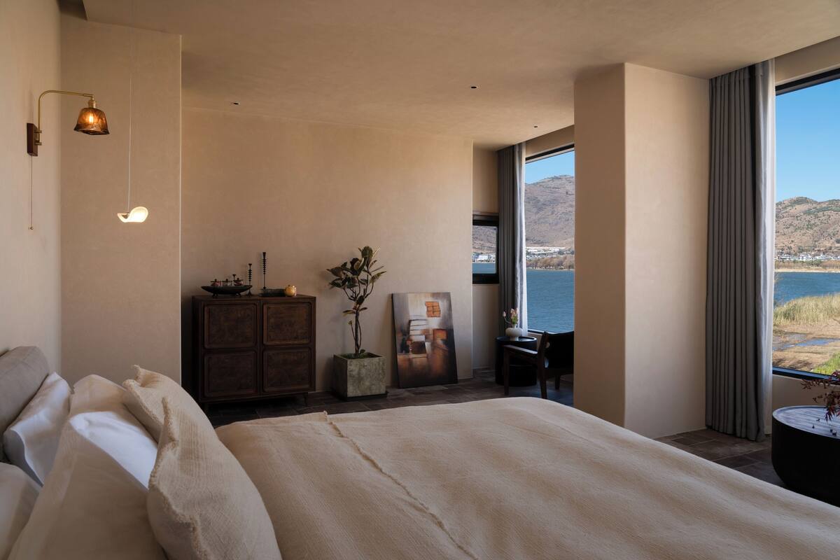 Un dormitorio con una cama grande, un escritorio, una planta en maceta y vistas a un lago y montañas.