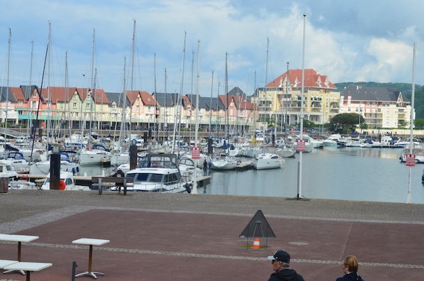 A marina with multiple boats docked, a variety of buildings in the background, and a clear sky.