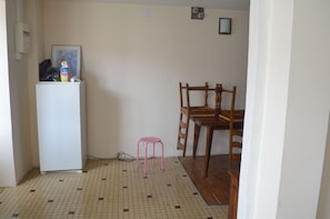 Une pièce avec un sol carrelé, un réfrigérateur blanc, une table à manger en bois avec des chaises et un petit tabouret rose.