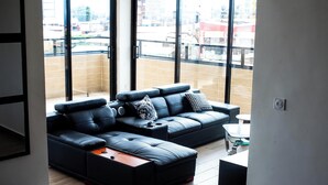 Un salon moderne avec un canapé en cuir noir, une petite table basse et une vue dégagée grâce à de grandes fenêtres.