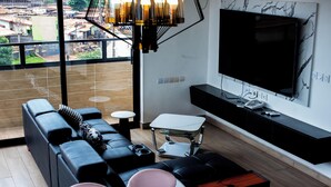 Un salon moderne avec un canapé, une petite table, un banc, un téléviseur et une vue sur l’extérieur.