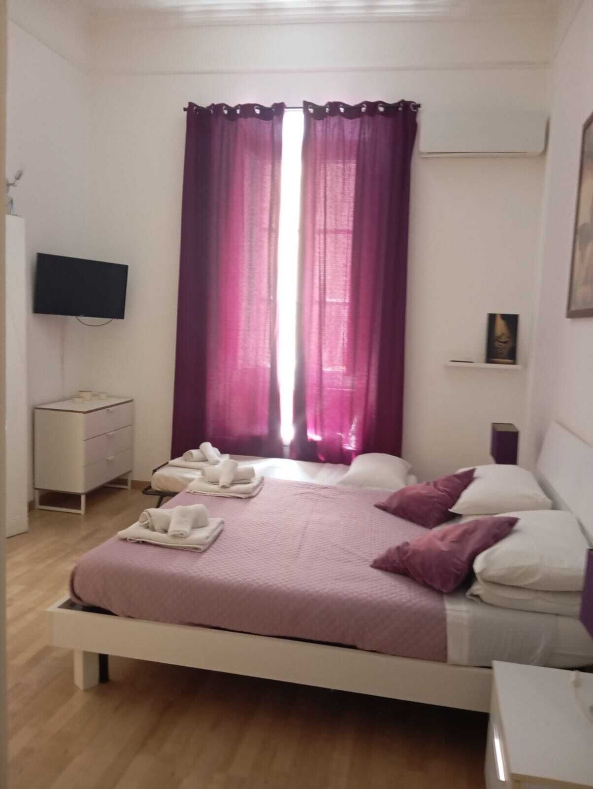 A bedroom with a bed, a TV, a nightstand, and a window with curtains.