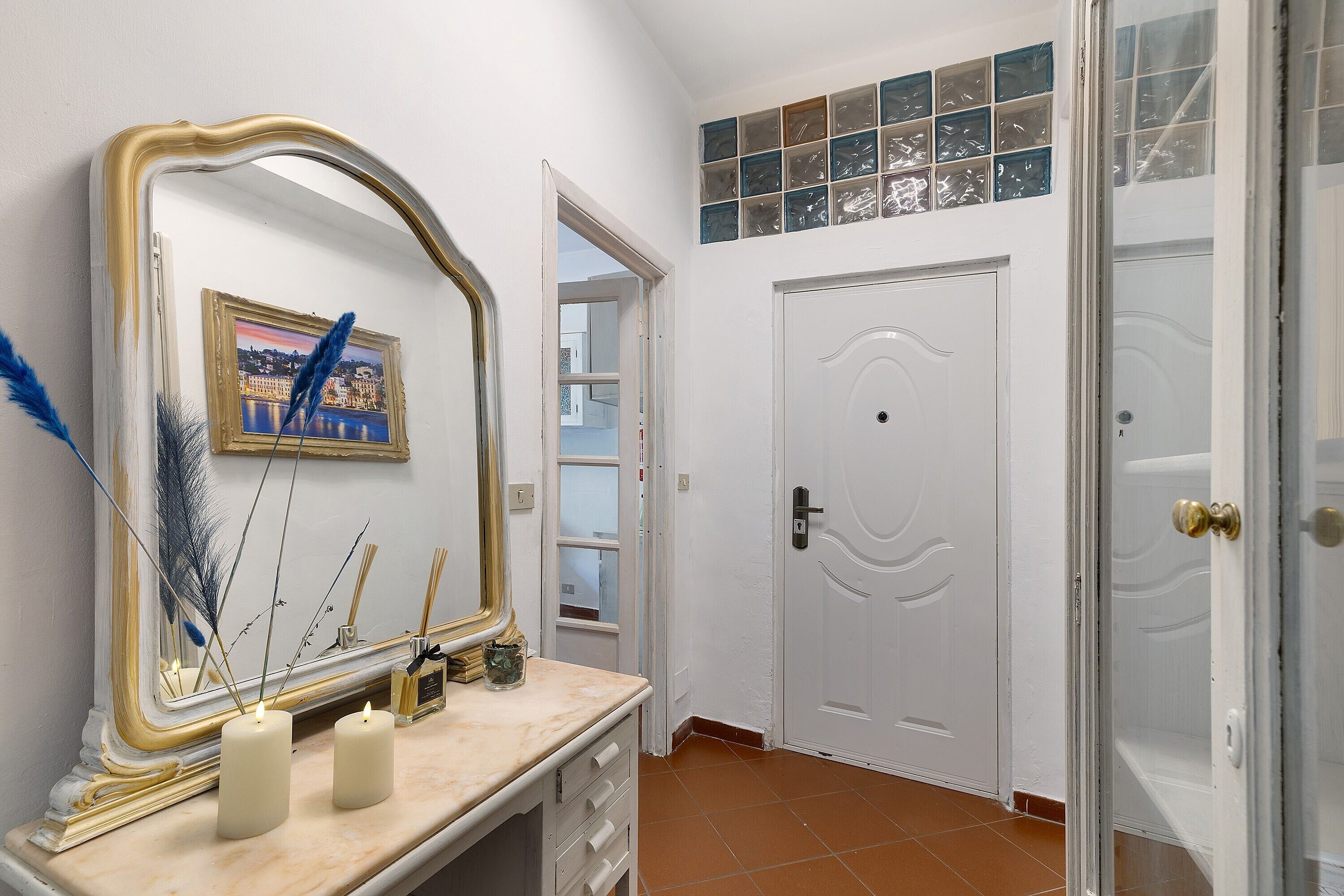 Une salle de bain avec un miroir, deux bougies, un tableau encadré et une porte.