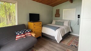 Een slaapkamer met een bed, een bank, een houten dressoir, een televisie en een raam met blinds.