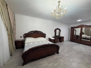 A bedroom with a wooden bed, a chandelier, a dresser, and a mirror. - Kol-Ukok Hotel (Bolshevik)