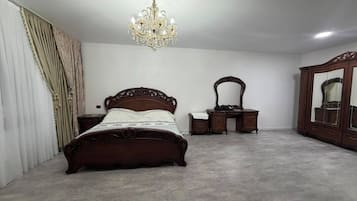 Quarto com uma cama grande, cômoda, espelho e lustre.