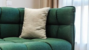En grøn sofa med en beige pude i et rum med trægulv og et vindue med gardiner.