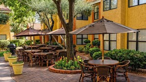 An outdoor patio with round tables and chairs, surrounded by potted plants and umbrellas. - Cozy 1-bedroom hotel with AC in charming Las Vegas (Las Vegas)