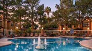 A pool with a fountain, surrounded by lounge chairs and umbrellas, with trees and buildings in the background. - Cozy 1-bedroom hotel with AC in charming Las Vegas (Las Vegas)