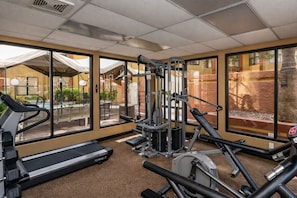 Ein Fitnessraum mit Trainingsgeräten, großen Fenstern und Blick auf Sitzmöglichkeiten im Freien.
