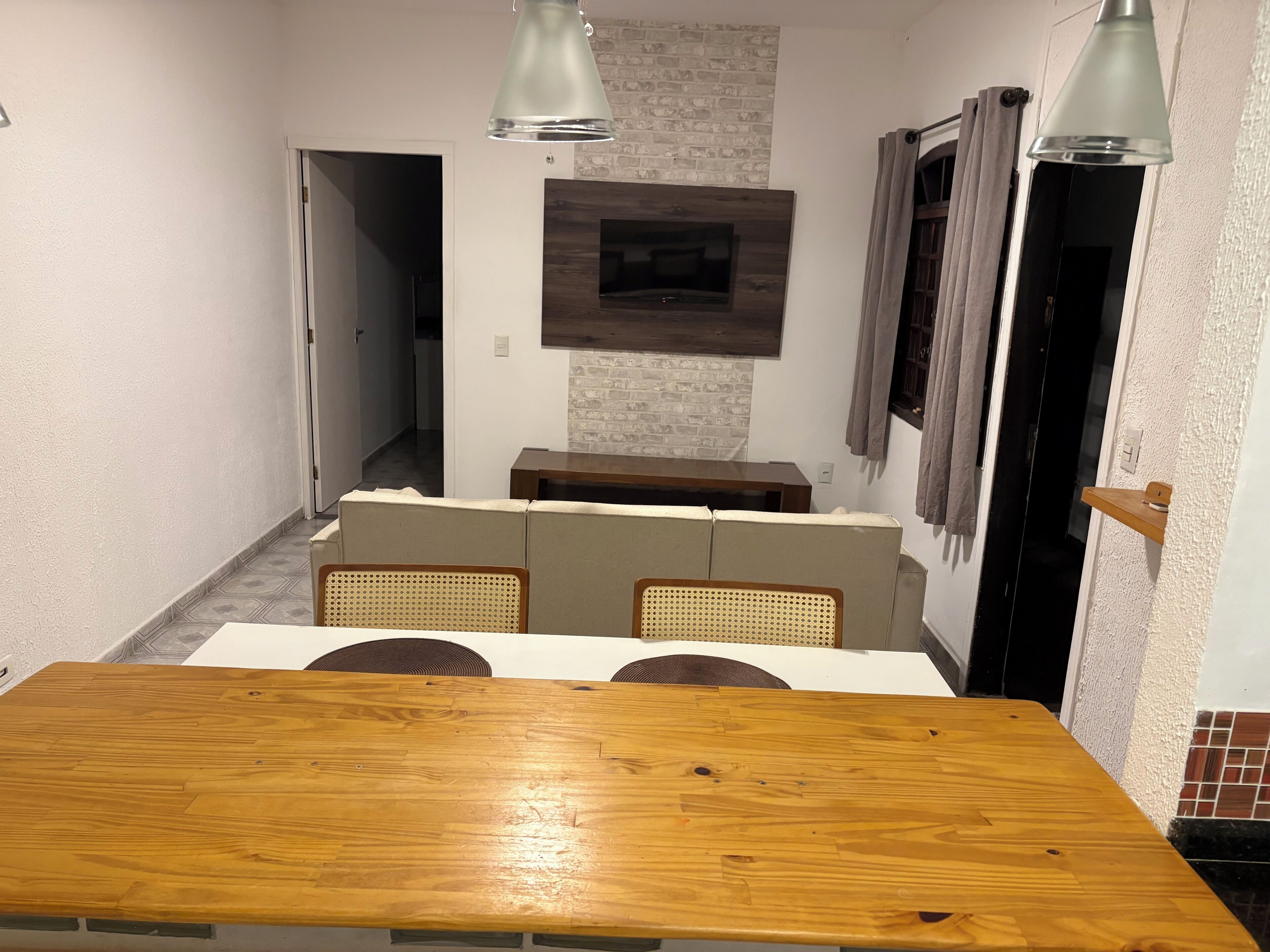 Ein Essbereich mit Holztisch, gepolsterten Stühlen, einer Couch und einem an der Wand montierten Fernseher.